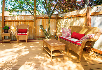 The pergola provides partial shade, while the deck features comfortable wicker furniture, including chairs, a loveseat, and a coffee table.